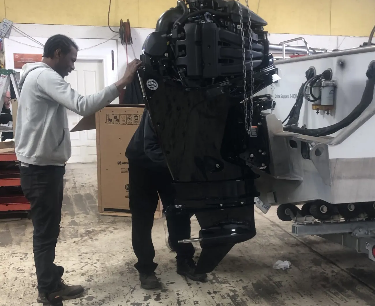 Two staff installing a large new outboard motor on an aluminum boat using a chain hoist