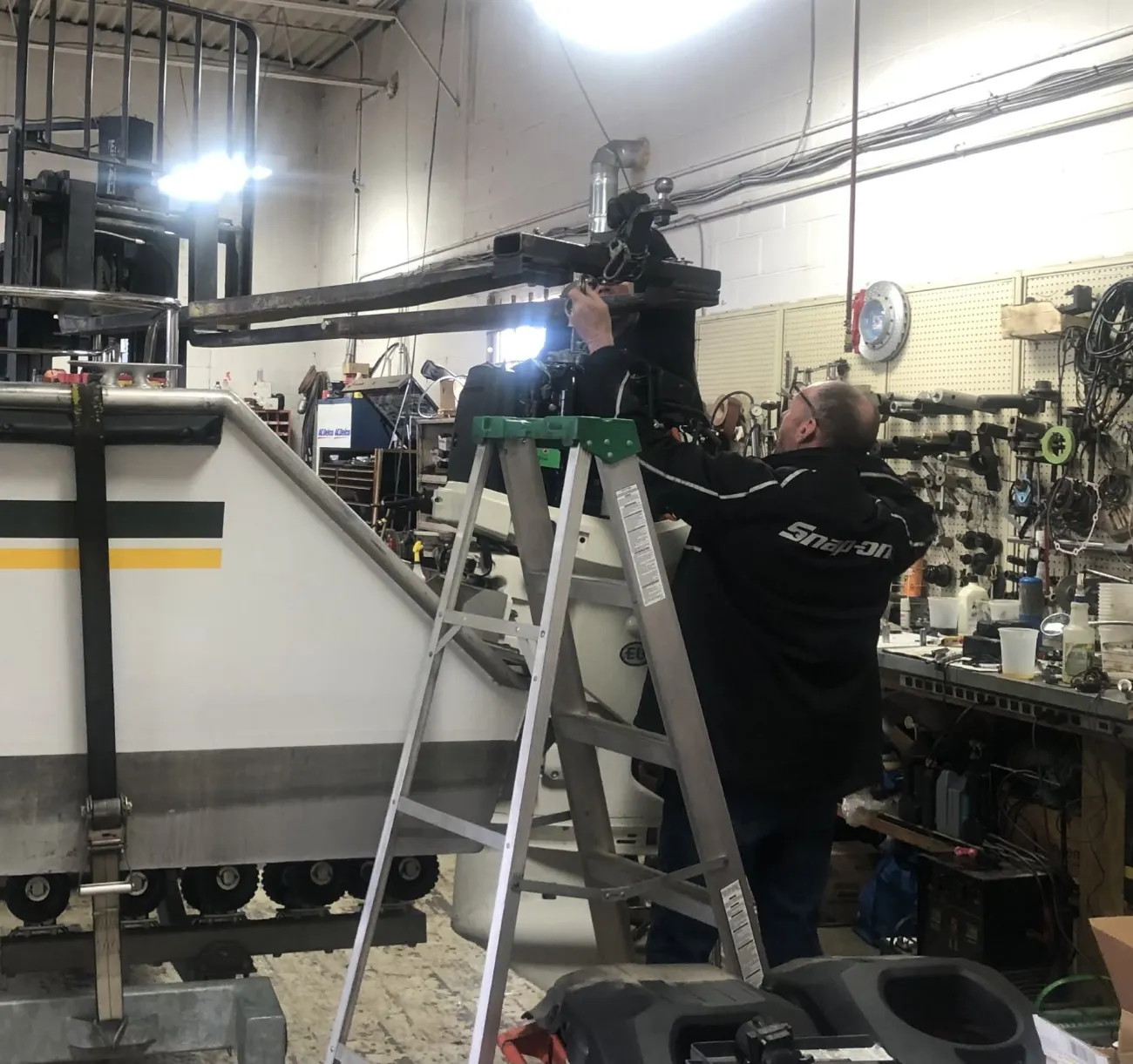 Technician on a ladder mounting an outboard motor to the transom of a boat on a trailer