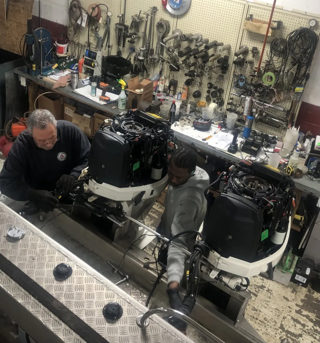 Two Hartzel Marine technicians servicing twin outboard motors with the cowls removed on a boat transom